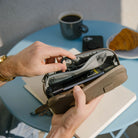 Person opening a CIVIC Access Pouch 0.5L in Fossil Brown on a table with a cup of coffee and croissant in the background Person opening a CIVIC Access Pouch 0.5L in Fossil Brown on a table with a cup of coffee and croissant in the background [13017a-FBN