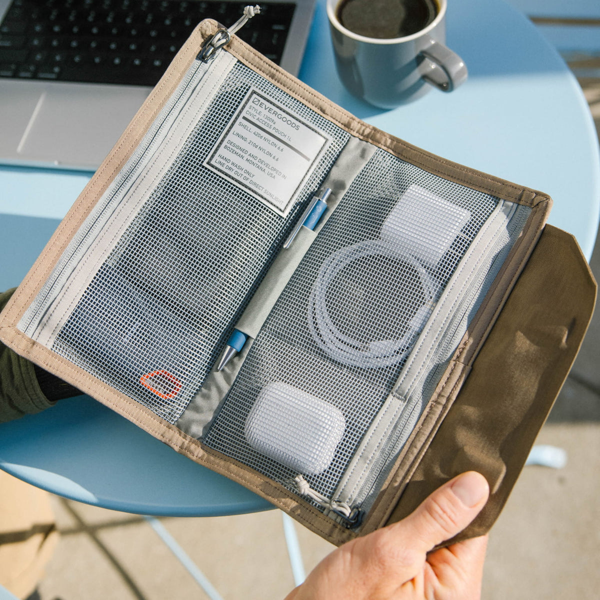 Hand holding a CIVIC Access Pouch 1L in Fossil Brown travel organizer with mesh pockets on a blue chair. [13009a-FBN]