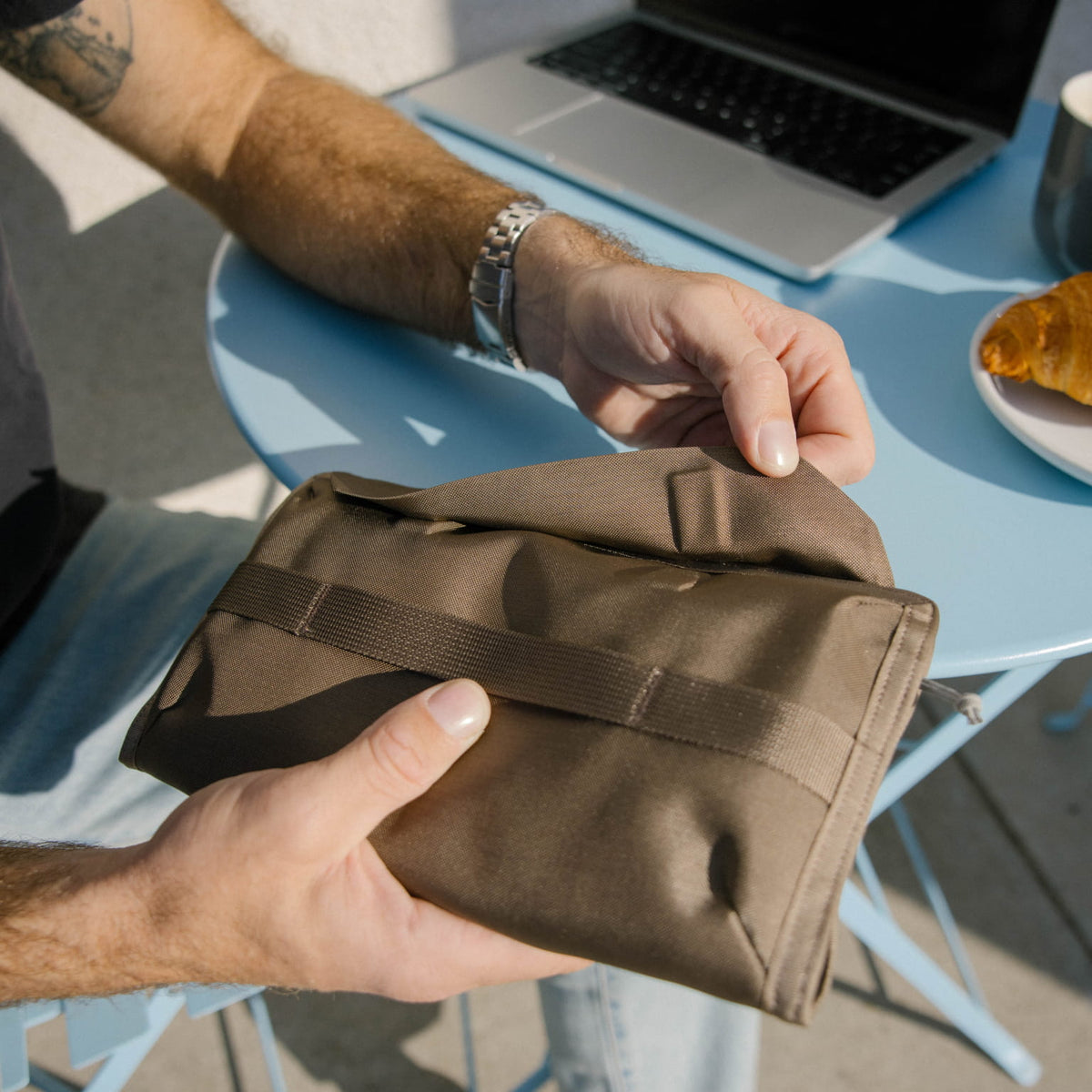 Person holding a CIVIC Access Pouch 1L in Fossil Brown with a laptop and food on a table in the background [13009a-FBN]