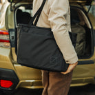CIVIC Daily Tote 24L in Solution Dyed Black - CDT24 - holding tote by trunk of car, shoulder carry CIVIC Daily Tote 24L in Solution Dyed Black - CDT24 - holding tote by trunk of car, shoulder carry [13024a-SBK