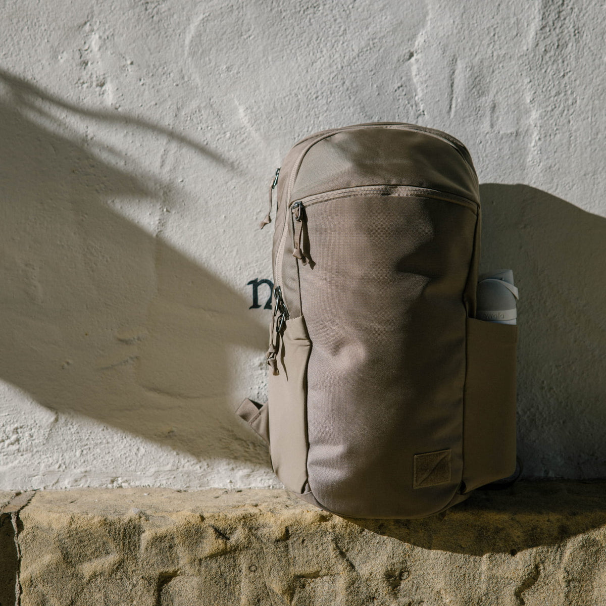 CIVIC Half Zip 22L in Fossil Brown backpack leaning against a textured wall [13003d-FBN]