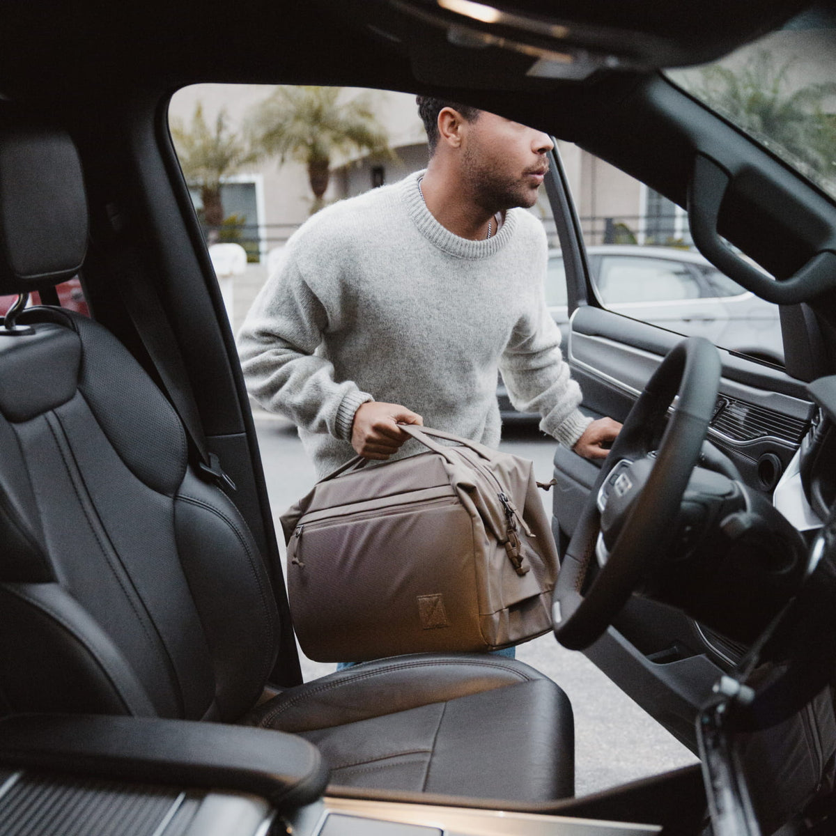 Man getting into a car with a Transit Duffel 25L in Fossil Brown , viewed from inside the vehicle. [13023d-FBN]