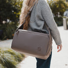 A woman in a gray sweater carries a taupe-gray nylon shoulder bag outdoors on a sunny day. A woman in a gray sweater carries a taupe-gray nylon shoulder bag outdoors on a sunny day. [13023d-FBN