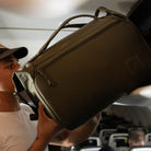Person pulling a Transit Duffel 25L in OD Green out of an overhead bin inside an airplane Person pulling a Transit Duffel 25L in OD Green out of an overhead bin inside an airplane [13023d-ODG