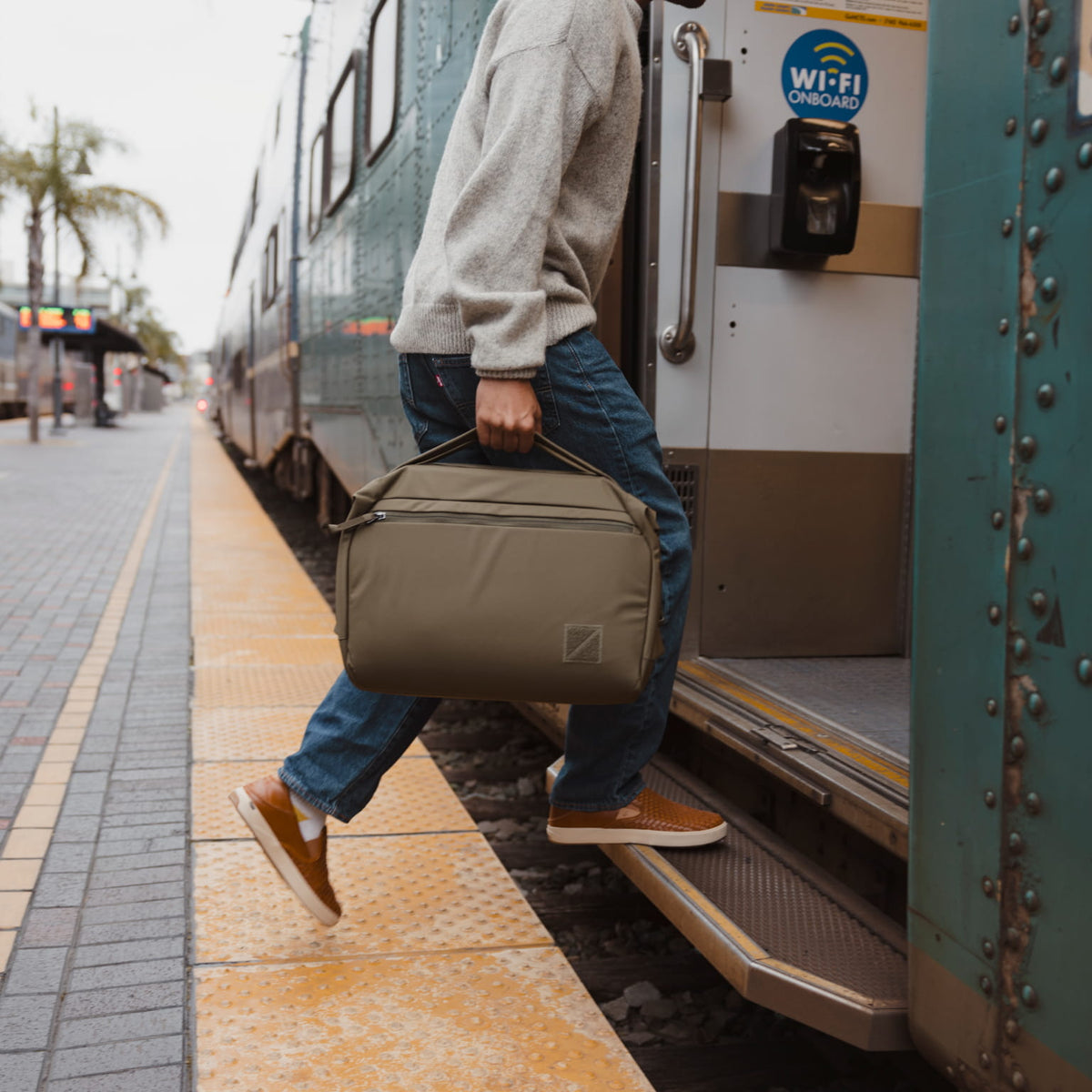 Person boarding a train with a Transit Duffel 25L in OD Green at a station platform visible [13023d-ODG]